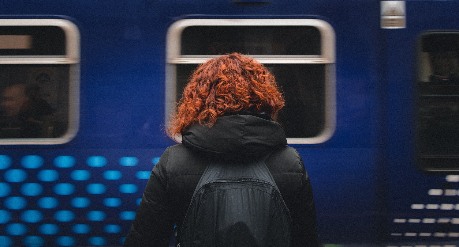 O femeie asteapta in gara, in timp ce un tren trece prin fata ei.